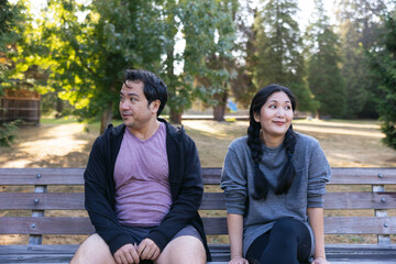 Awkward adults sitting on park bench together.