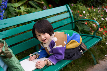 Asian little boy drawing peacefully on a bench in a beautiful garden