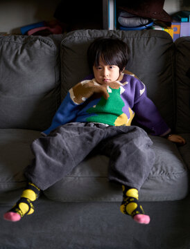 Asian little boy sulking lying on sofa