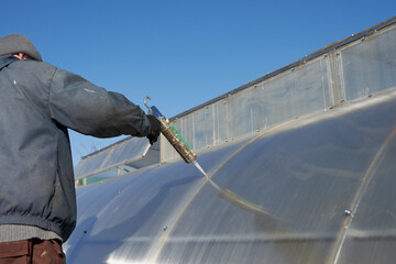 A man seals holes on a polycarbonate greenhouse with a silica sealant from fixing screws.