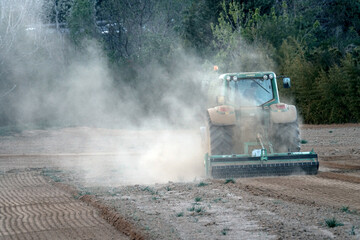 Tractor ploughing a field shrouded in the dust of dry soil from the long drought. Pianezza, Italy - April 2023