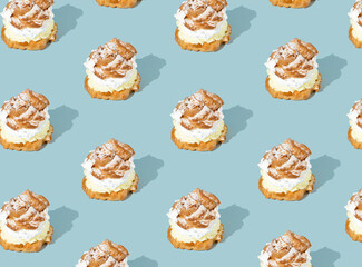 Trendy sunlight summer pattern made with cream puffs on blue background. Minimal food concept. Cream puffs filled with pastry cream and sprinkled with powdered sugar.