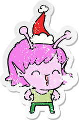 distressed sticker cartoon of a alien girl laughing wearing santa hat