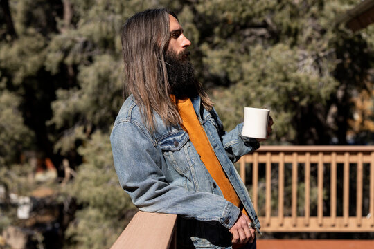 Man with long hair on porch in nature with coffee