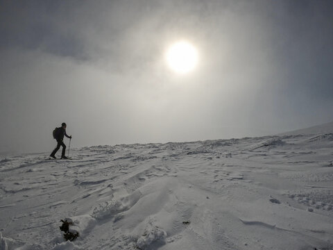back country skier is going uphill on a windswept part of mountain