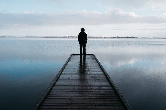 Young man stands on end of wooden jetty in Iceland