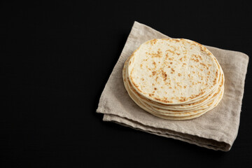 Stack of Whole Wheat Flour Tortillas on a black background, side view. Copy space.