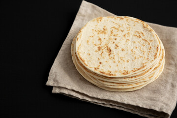 Stack of Whole Wheat Flour Tortillas on a black background, side view. Copy space.