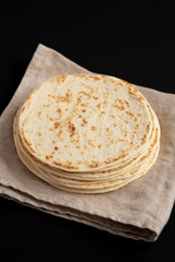 Stack of Whole Wheat Flour Tortillas on a black background, side view.