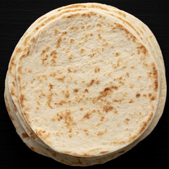 Stack of Whole Wheat Flour Tortillas on a black background, top view. Flat lay, overhead, from above.