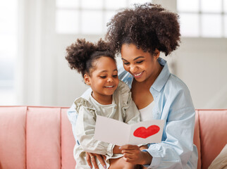 Cute little daughter giving his mom greeting postcard on Mother's day, celebrating together at home