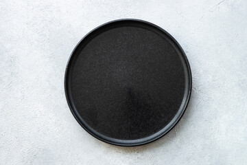 Black plate on white stone table. Empty plate top view.