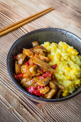 Saffron rice with pieces of chicken and vegetables on wooden table.