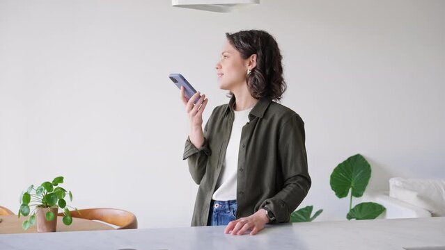 Smiling Brunette Young Woman using smart phone Recording Warm Voice Message to someone special, Loved One, Friend or Partner in Cozy Home Setting. Remote communication and connection in modern life