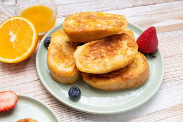 Torrijas, Spanish Style French Toast Served With Orange Topping, Glaze, Fresh Blueberries, Strawberry On Green Plate, Wooden Table. A Half Of Orange. Spanish Dessert. Horizontal plane
