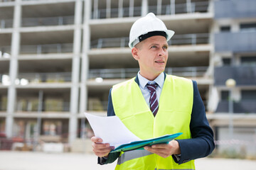 Civil engineer standing on a construction site, carefully studies important work documents