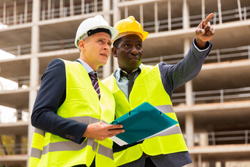 African-american civil engineer discussing a construction plan with a young colleague shows him...