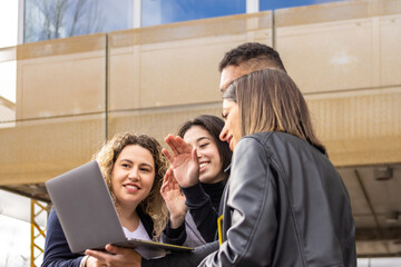 Fototapeta premium Group of young entrepreneurs using a laptop in the street. Young entrepreneurs making a video call on a laptop outdoors
