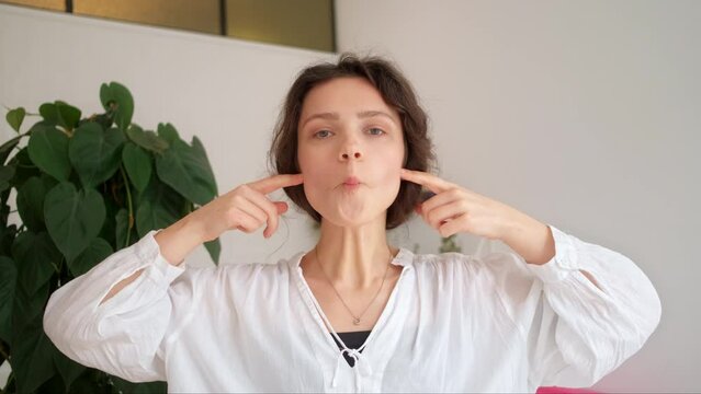 Young attractive 30 year old woman showing how to do facial massage for cheeks cheekbones at home. Easy tutorial learning to give relaxing face massage exercises for youthful glowing complexion UGC