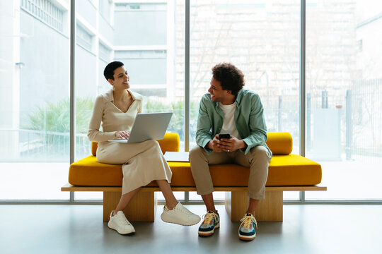 Coworkers discussing project sitting on yellow sofa in a workspace