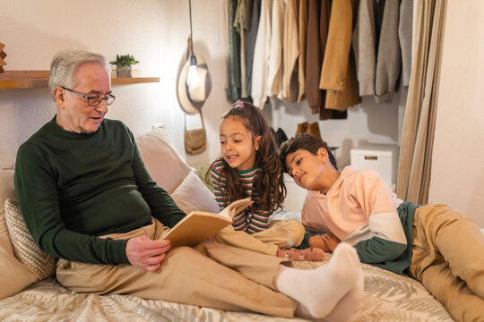 grandfather with grandchildren reading a book in bed