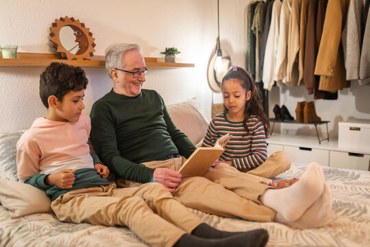 grandfather with grandchildren reading a book in bed