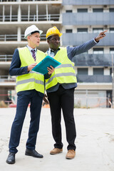 African-american civil engineer discussing a construction plan with a young colleague shows him something, pointing is it