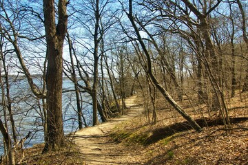 Springtime landscape of hiking trail passing between forest of bare trees and the Illinois River at Starved Rock State Park, near Oglesby, IL.