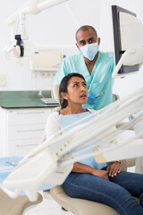Latin american dentist talking to woman during dental checkup, discussing teeth x-ray and treatment...
