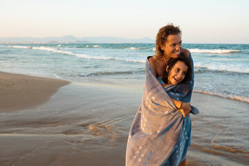 Mother and daughter wrapped in a towel smiling in the beach
