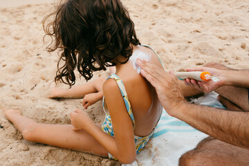 Man applying sunscreen on daughter's back in the beach