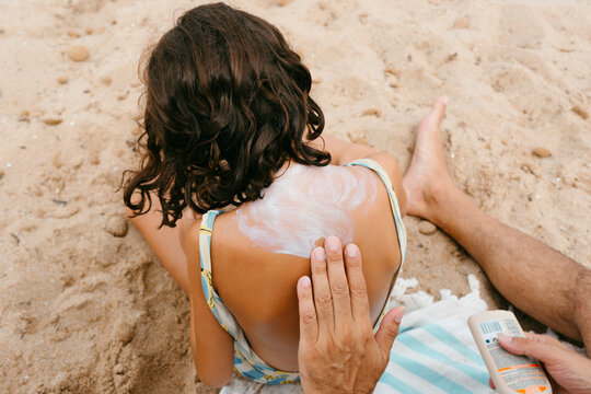 Father applying sunscreen on daughter's back in the beach