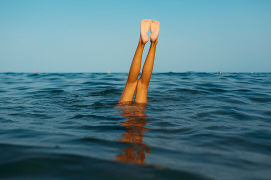 Anonymous child's legs doing handstand in the sea water