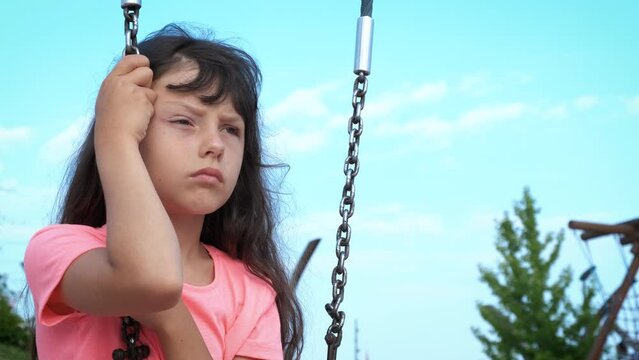 Sad child expresion on courtyard. A view of little girl with sad feelings sitting on swing at courtyard.
