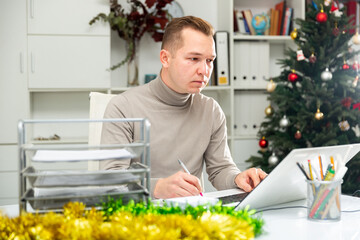Man bookkeeper doing paperwork in his workplace in Christmas decorated office.