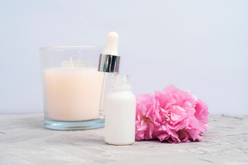 White serum dropper bottle, pink cherry blossom and aroma candle on concrete background. Closeup, front view