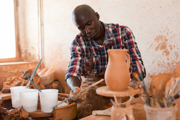 Professional African American male potter painting ceramic pot in pottery workshop