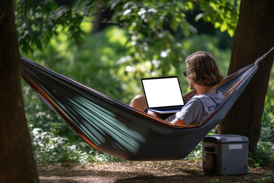 A man works on a laptop while lying in a hammock outdoor in nature. Generative ai