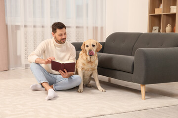 Man reading book on floor near his cute Labrador Retriever at home