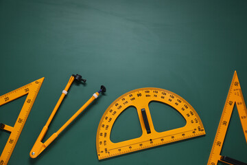Protractor, triangles and compass on green chalkboard, flat lay. Space for text
