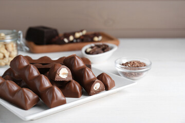 Tasty chocolate bars with nuts on white wooden table, space for text