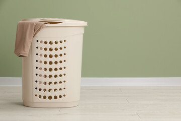 Plastic laundry basket with clothes near light green wall. Space for text
