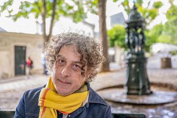 Portrait of a man traveling in Paris, France, in the Montmartre neighborhood. A pretty fountain is...