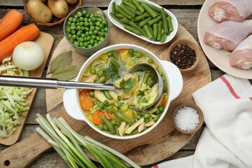 Saucepan of delicious vegetable soup with chicken and different ingredients on wooden table, flat...
