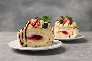 Pieces of tasty meringue roll with jam, cream, strawberry, blueberry and mint on light grey table, closeup