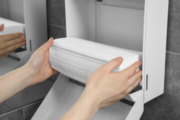 Woman putting new fresh paper towels into dispenser in bathroom, closeup
