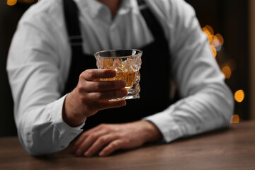 Bartender with glass of whiskey at bar counter indoors, closeup