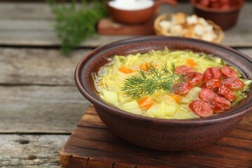 Bowl of delicious sauerkraut soup with smoked sausages and dill on wooden table, closeup