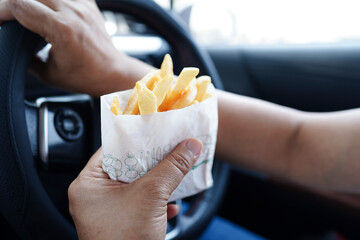 Asian woman driver hold and eat french fries in car, dangerous and risk an accident.