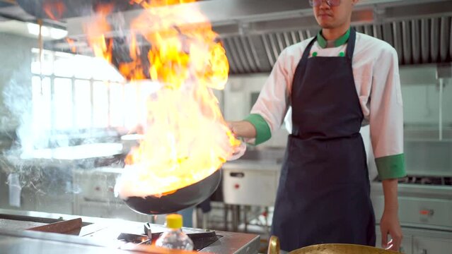 Asian professional chef cooking with a fire in kitchen in Asian restaurant.